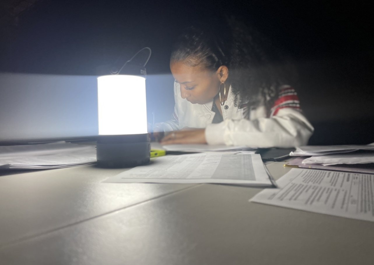 Chelsea working through paperwork by lantern light while producing a music video